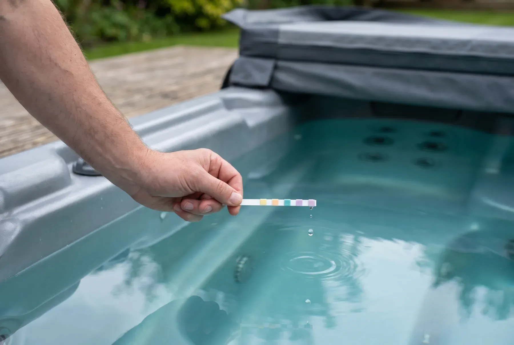 A hand holding a hot tub test strip above clear water