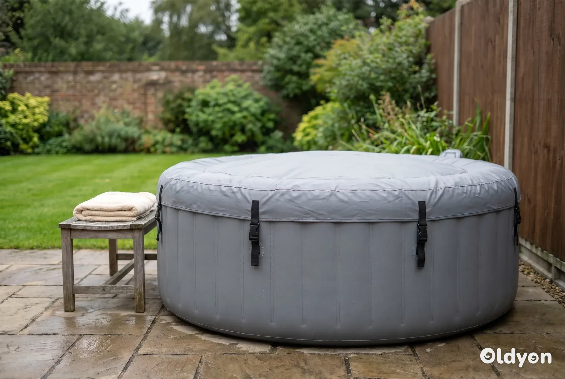 Rund oppustelig udespa med et gråt isoleret cover på en plan flisebelagt terrasse i en grøn britisk have
