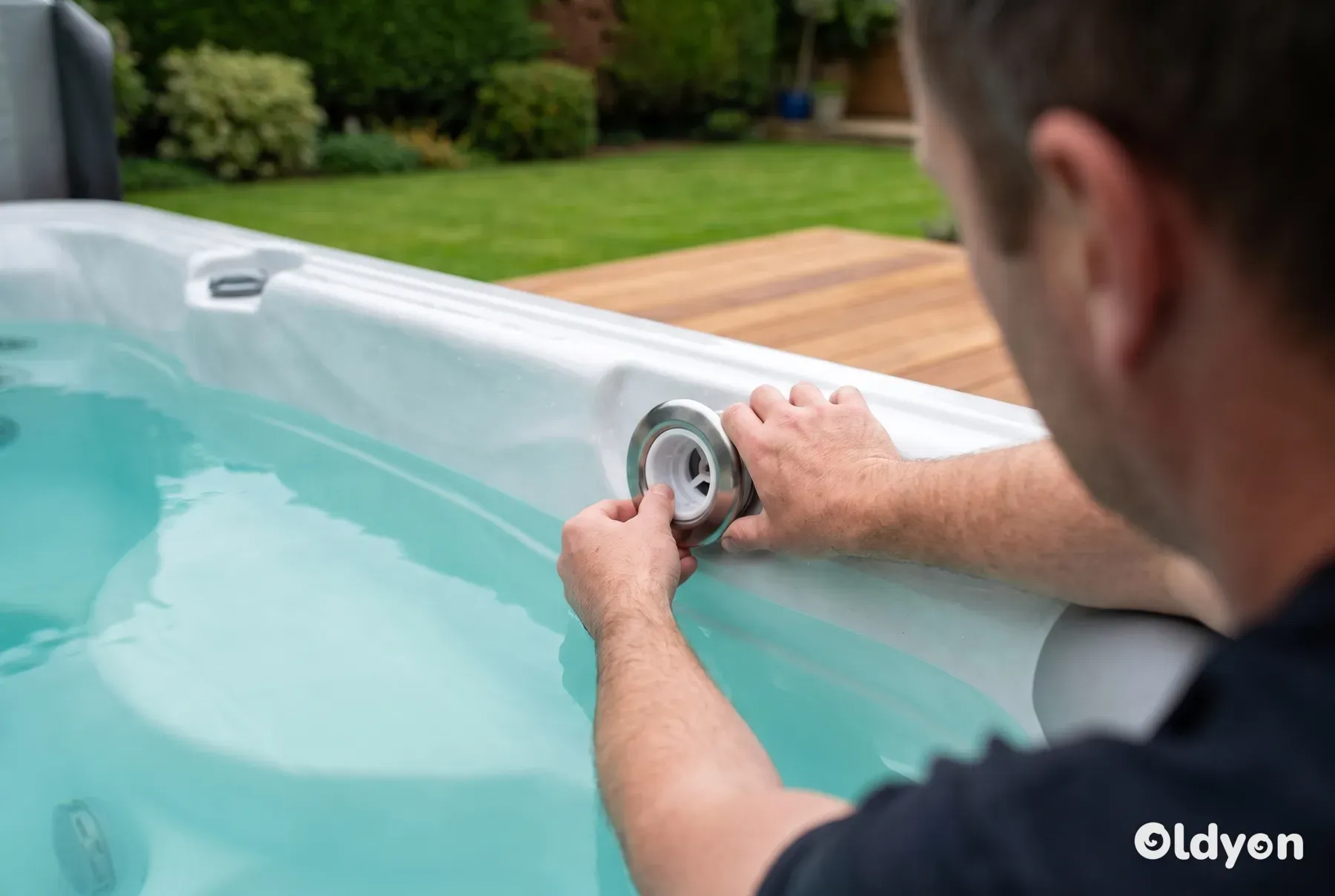 Hands seen from behind refitting a stainless steel jet insert into a white hot tub shell in a British garden