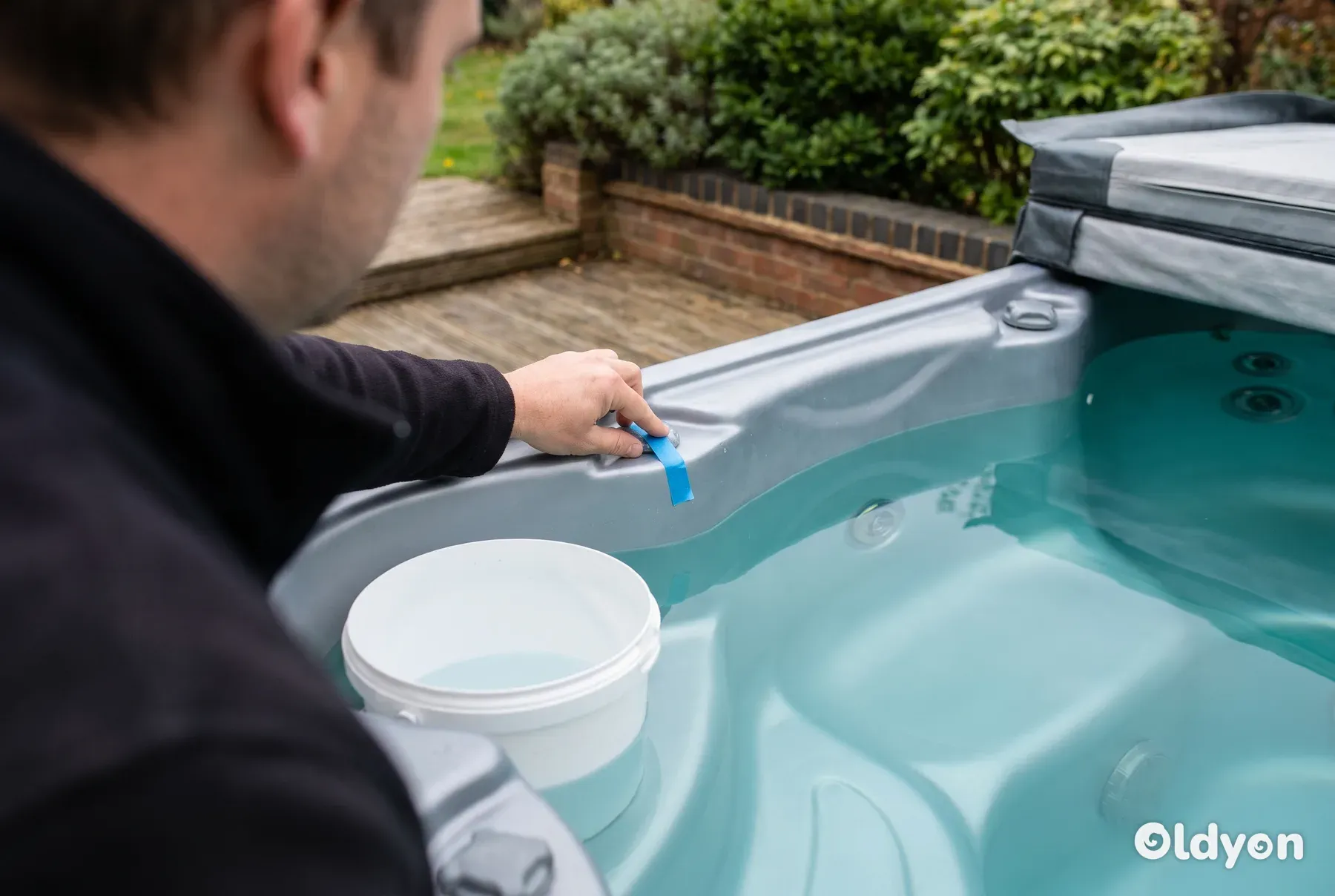 Bucket standing on the inside step of an open hot tub in a British garden, set up for a water loss test