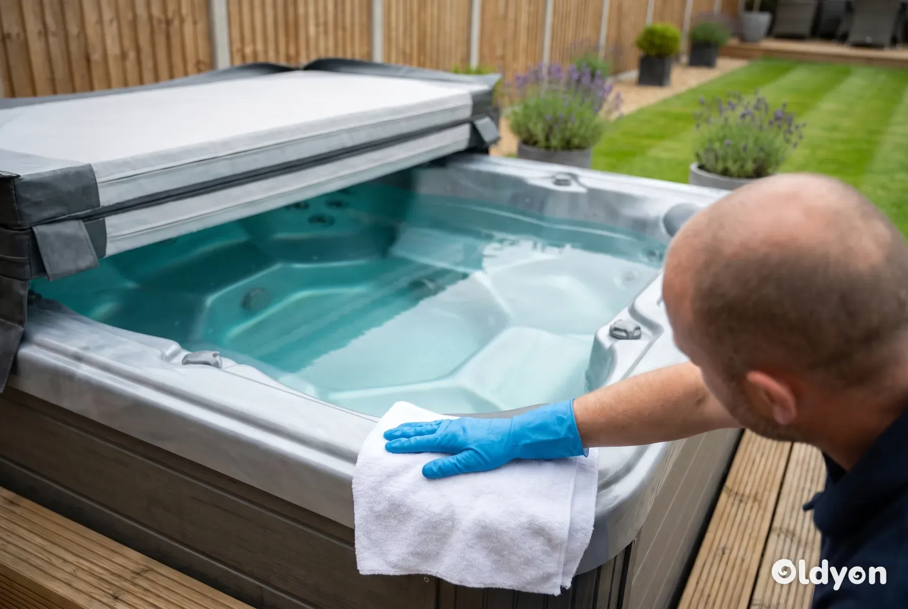 Gloved hand wiping the waterline of a clean hot tub with a soft cloth in a green British garden