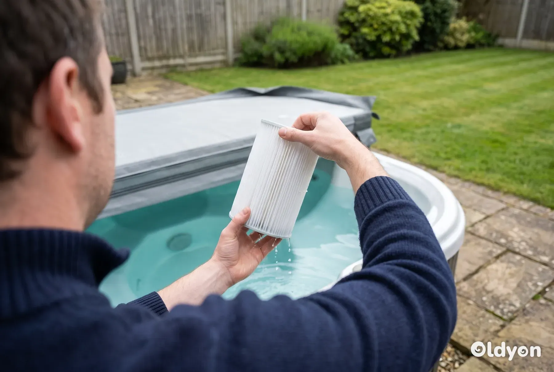 Hände, die eine saubere Faltenfilterkartusche neben einem offenen Whirlpool mit klarem Wasser in einem britischen Garten anheben