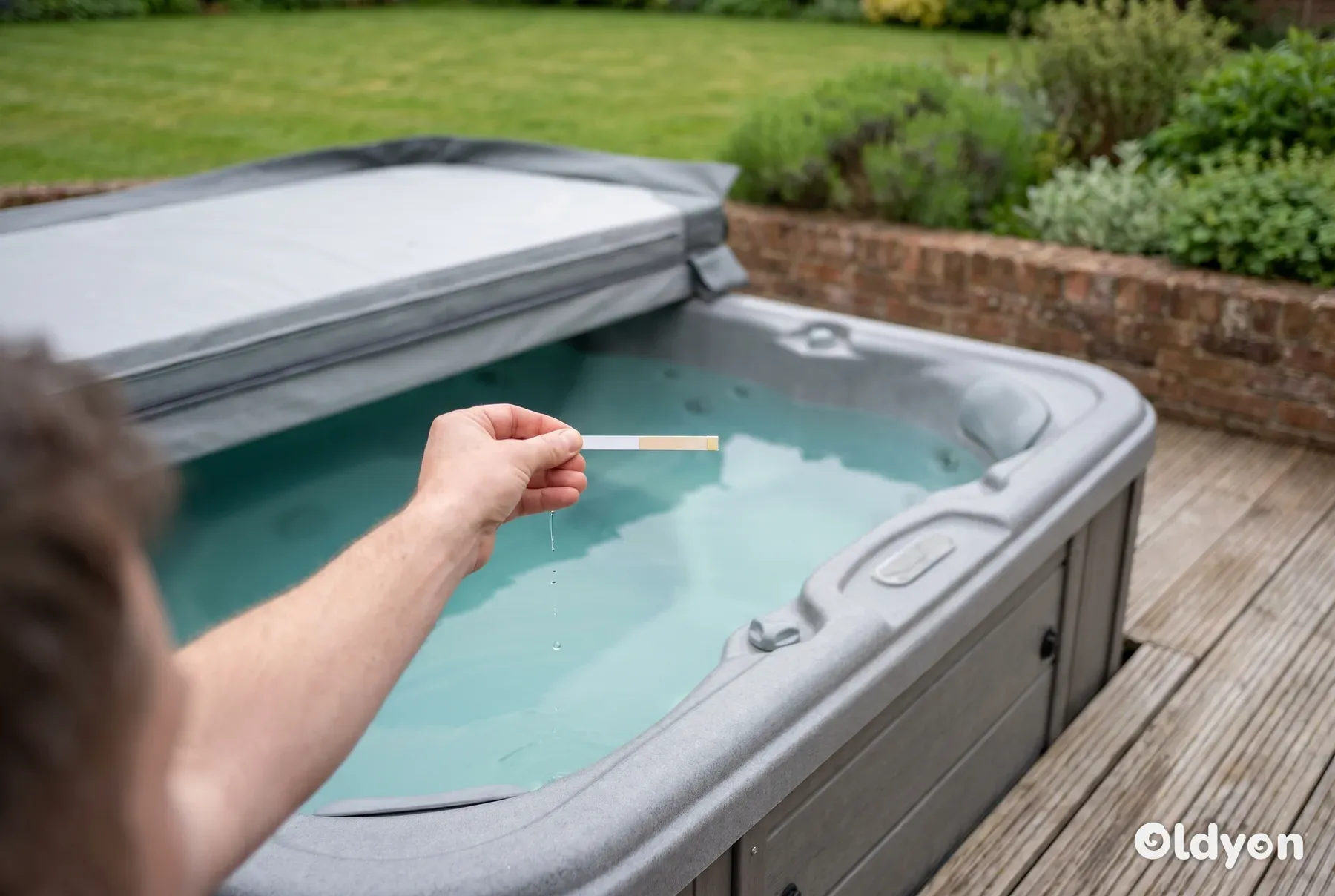 Eine Hand hält einen Wasserteststreifen über einen klaren Whirlpool auf einer Holzterrasse in einem grünen britischen Garten