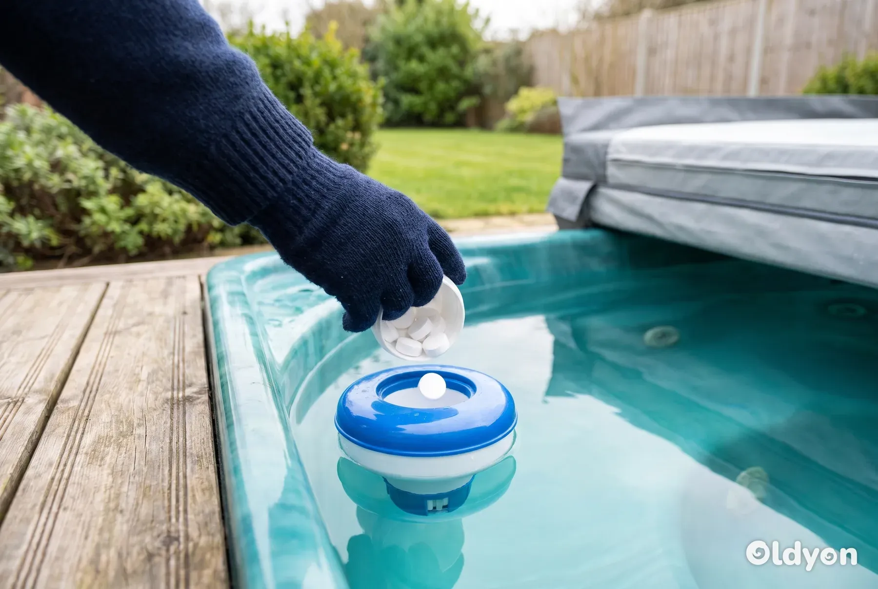 Eine behandschuhte Hand legt weiße Bromtabletten in einen Dosierschwimmer in einem Whirlpool in einem britischen Garten