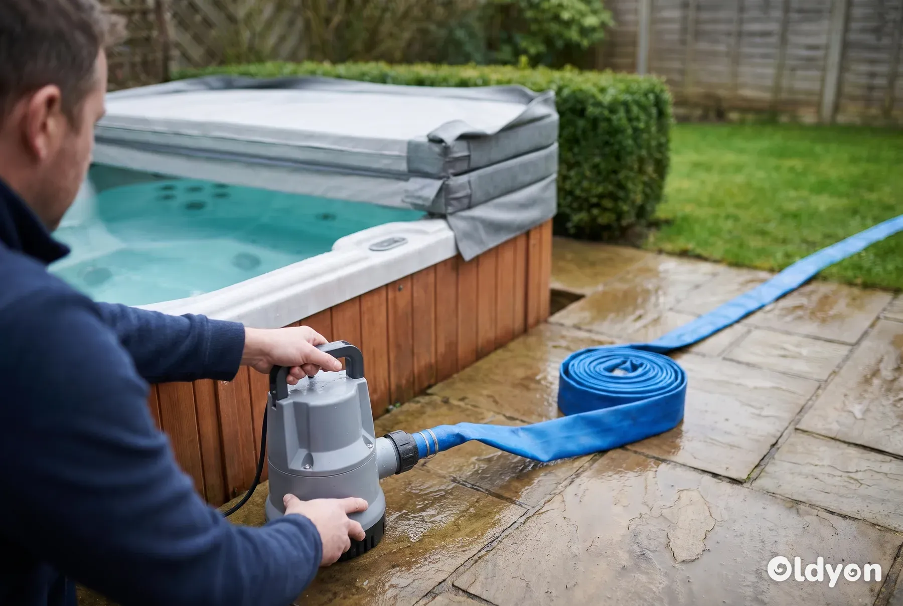 Entwässerungstauchpumpe mit blauem Flachschlauch auf einer Gehwegplatte neben einem Whirlpool in einem britischen Garten