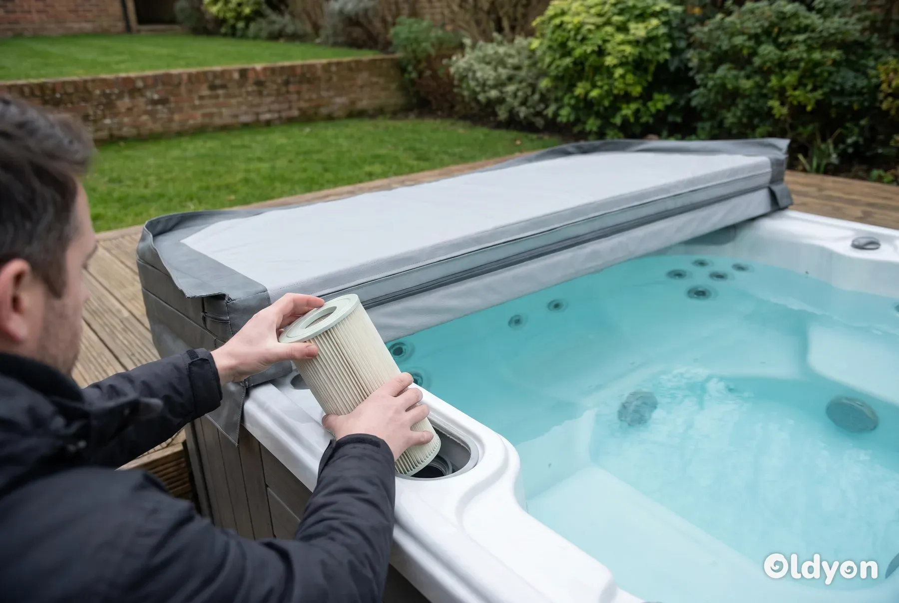 Des mains retirant une cartouche filtrante du boîtier de filtre d'un spa sur une terrasse en bois dans un jardin britannique