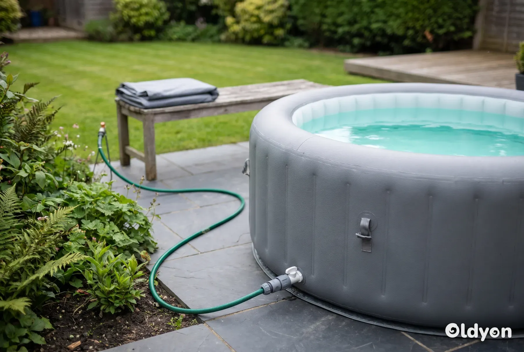 Garden hose connected to the drain valve of an inflatable hot tub on a paved patio in a British garden