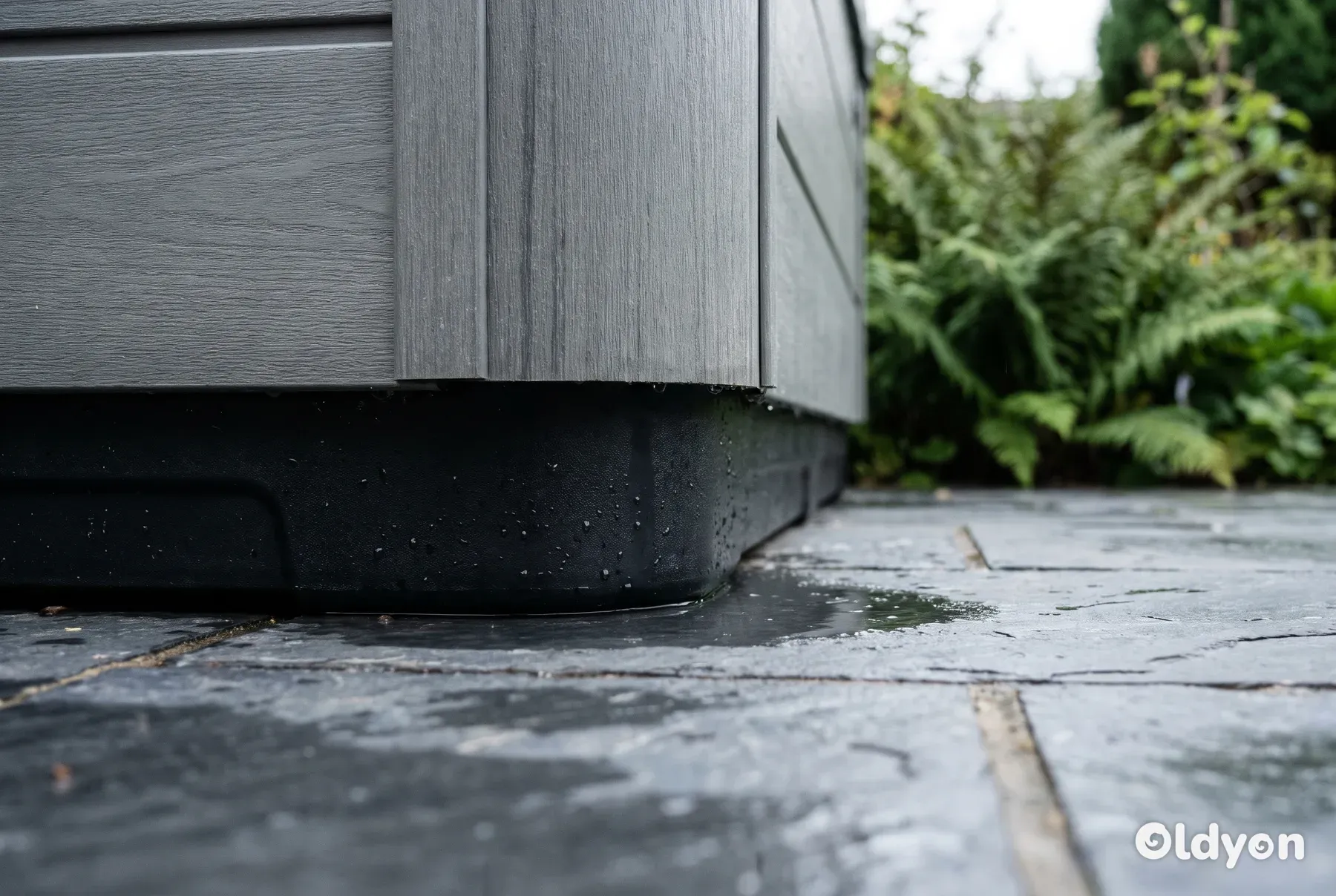 Den syntetiske bund på et udespa står fuldstændig upåvirket af en pyt med regnvand på en terrasse.