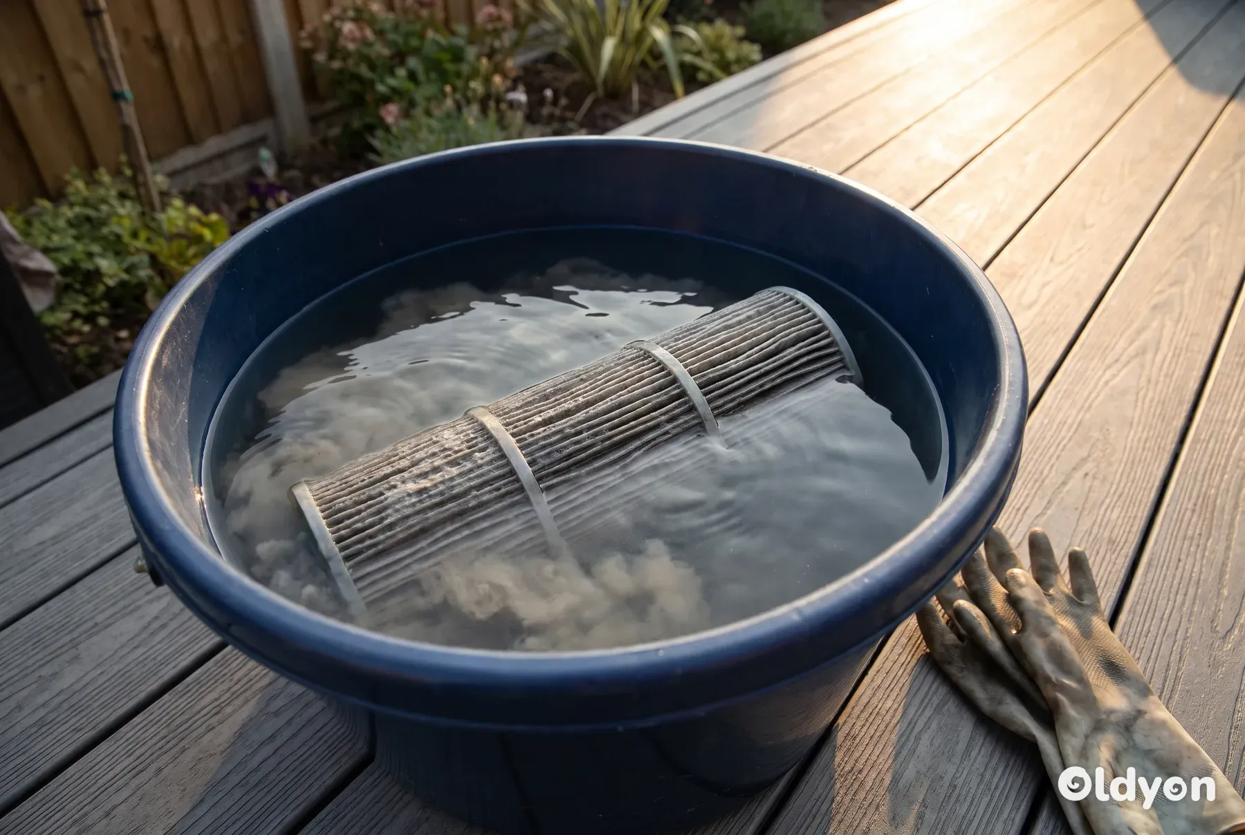 Un filtro a cartuccia per vasca idromassaggio completamente immerso in un grande secchio di plastica con acqua su una pavimentazione in materiale composito.