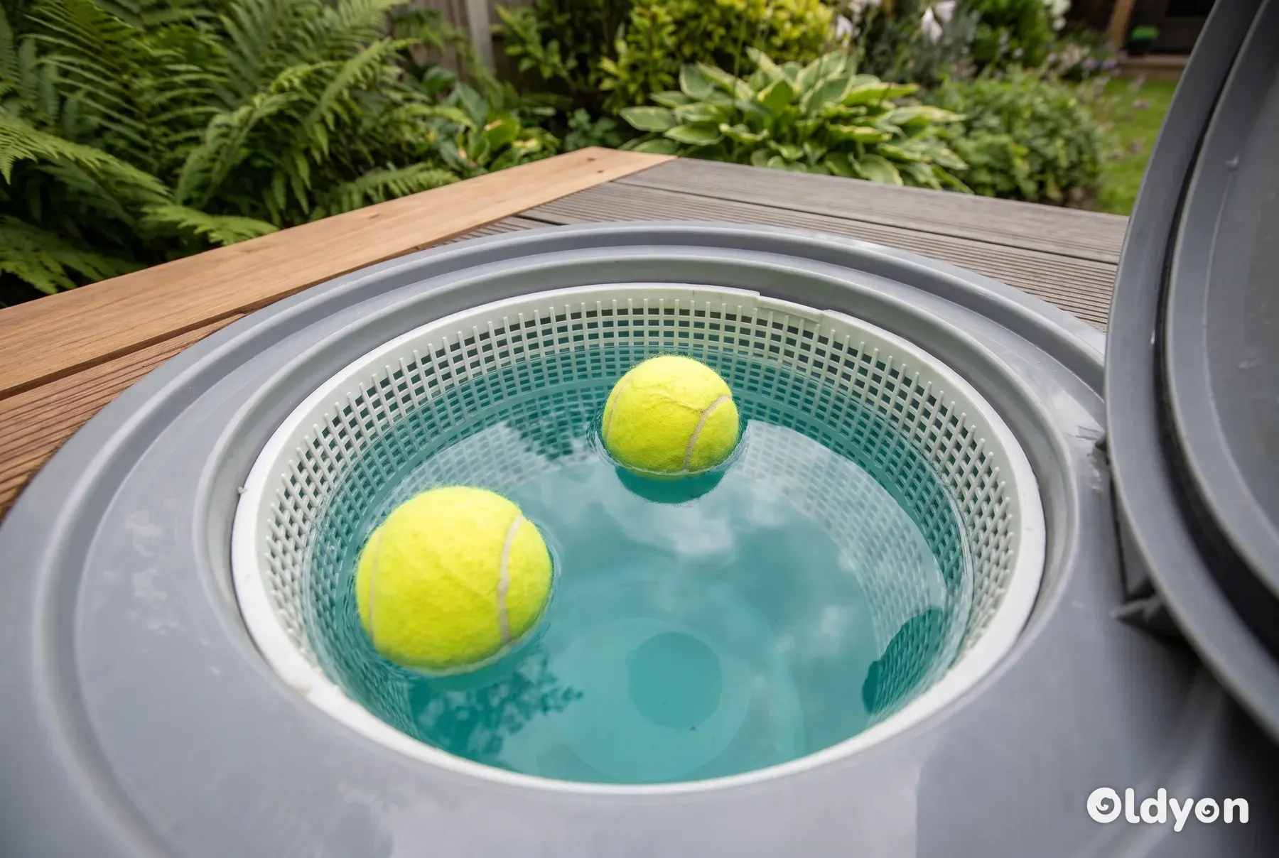 Due palline da tennis giallo acceso che galleggiano all'interno del cestello dello skimmer in plastica grigia di una vasca idromassaggio.