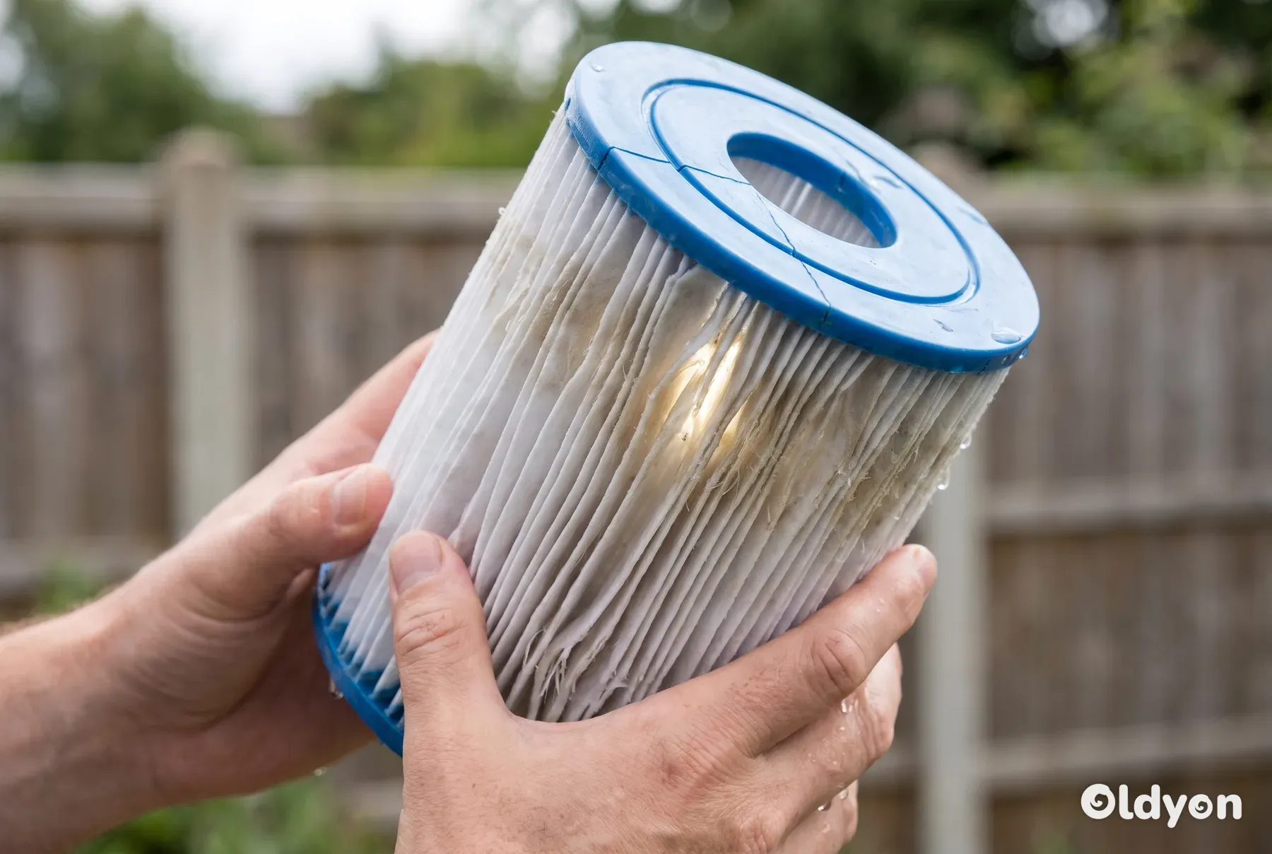 Un primo piano di un filtro per vasca idromassaggio danneggiato che mostra pieghe in tessuto sfilacciate e appiattite e un tappo terminale in plastica crepato.