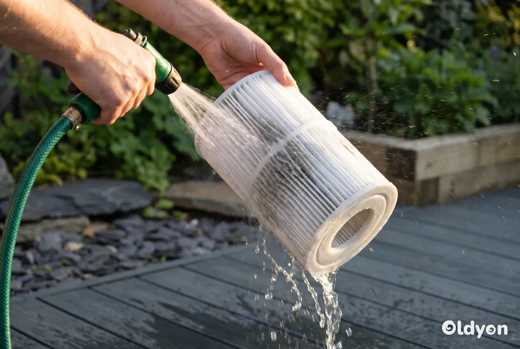 Delle mani usano un tubo da giardino per spruzzare via con forza lo sporco da una cartuccia pieghettata del filtro della vasca idromassaggio.