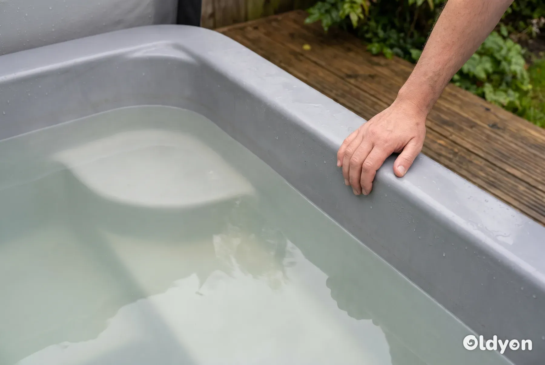 Una mano è appoggiata con cautela sul bordo di una vasca idromassaggio piena di acqua opaca, lattiginosa e non sicura.