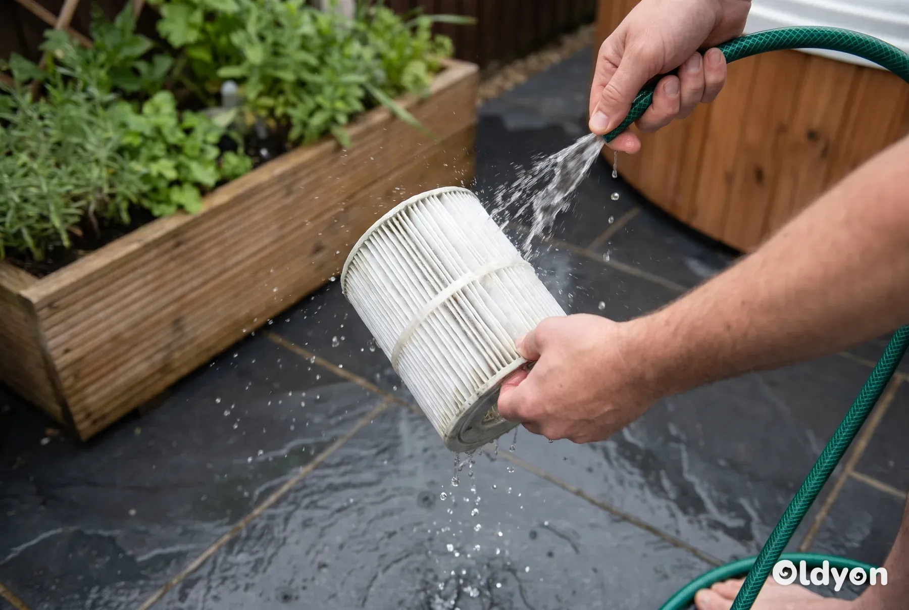 Una persona che usa un tubo da giardino per risciacquare le pieghe di una cartuccia del filtro della vasca idromassaggio.