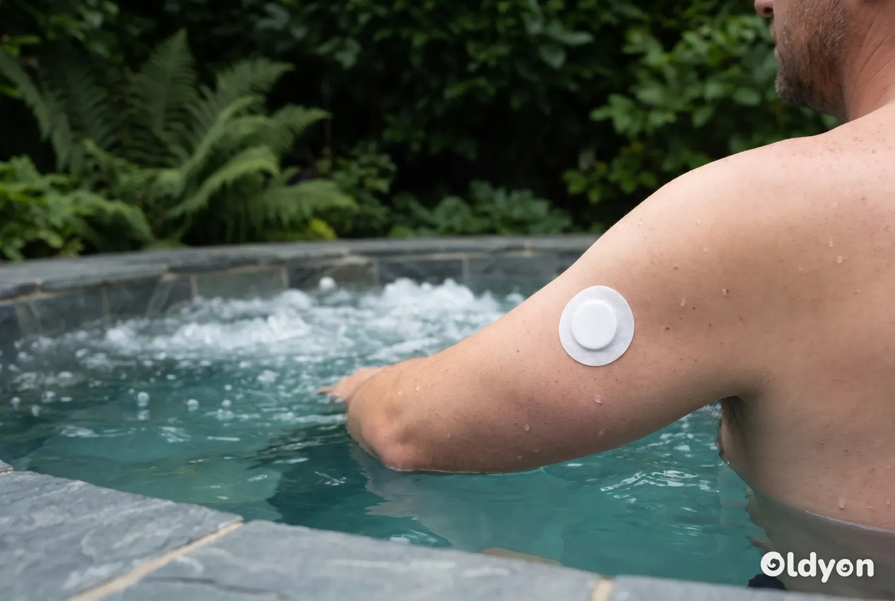 En person i et spabad holder sin arm med et sensorplaster sikkert over det boblende vand.