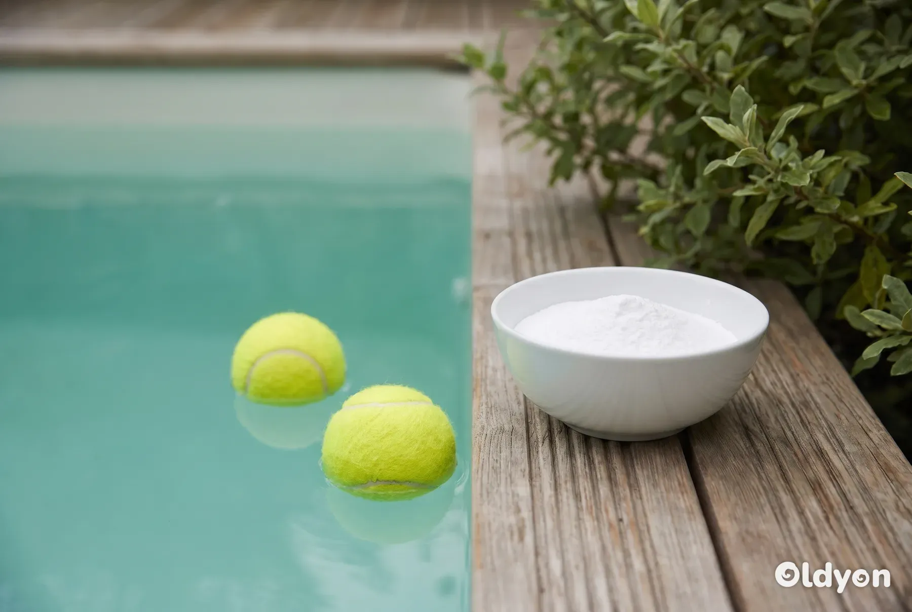 Twee gele tennisballen drijven in het water naast een eenvoudige kom met wit poeder.