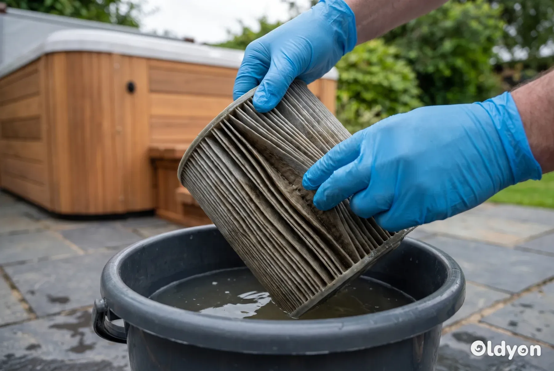 Handskebeklædte hænder undersøger et beskidt spafilter med misfarvede lameller over en spand vand.