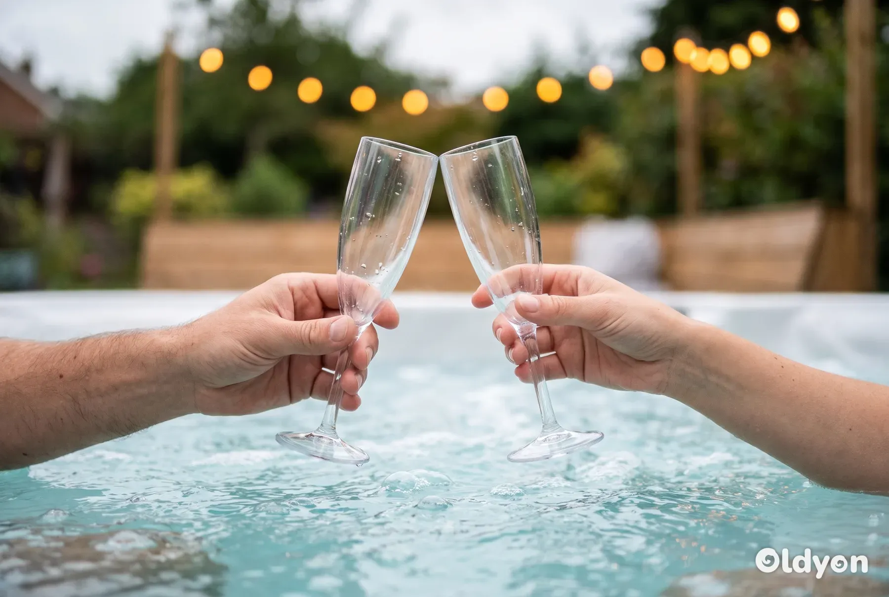 Due mani sollevano e fanno tintinnare dei flûte da champagne in plastica trasparente appena sopra l'acqua gorgogliante della vasca idromassaggio.