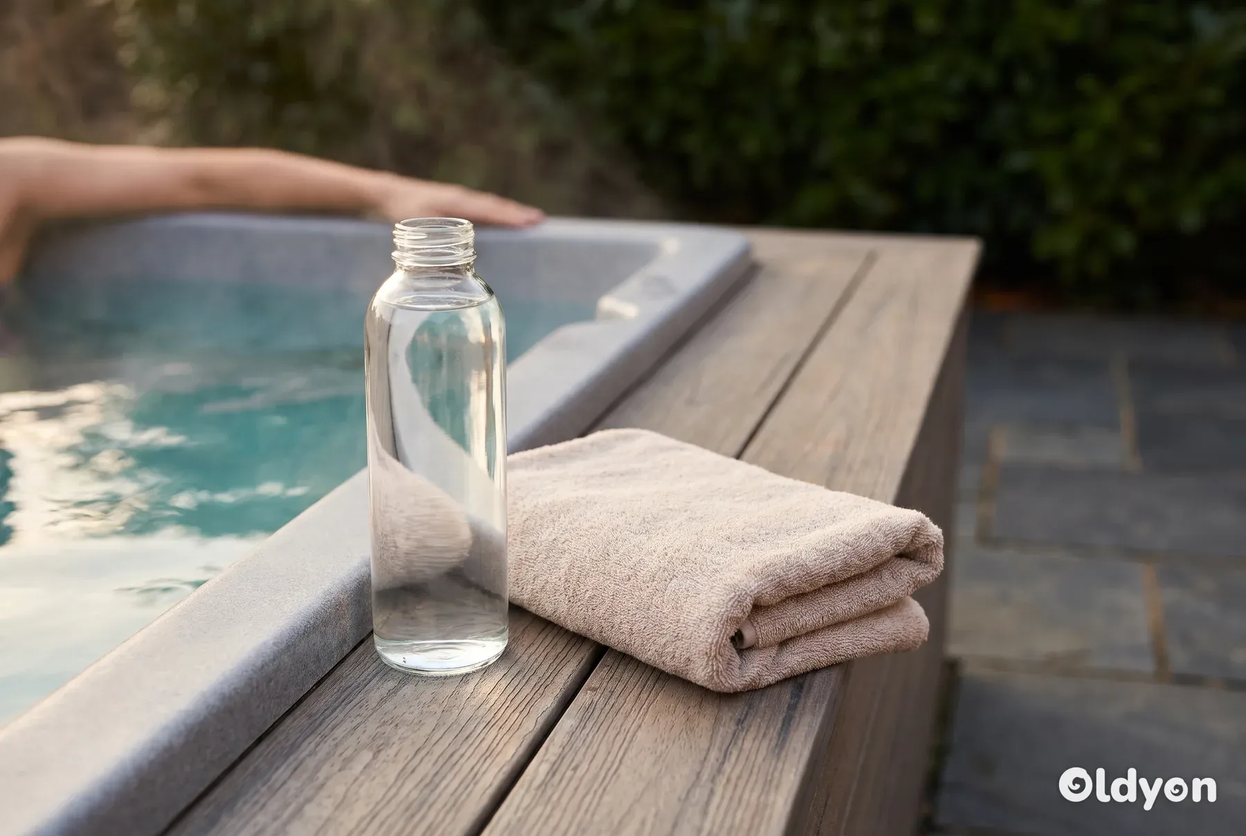 Una bottiglia d'acqua trasparente e un asciugamano piegato poggiano sulla pavimentazione in legno accanto a una vasca idromassaggio.