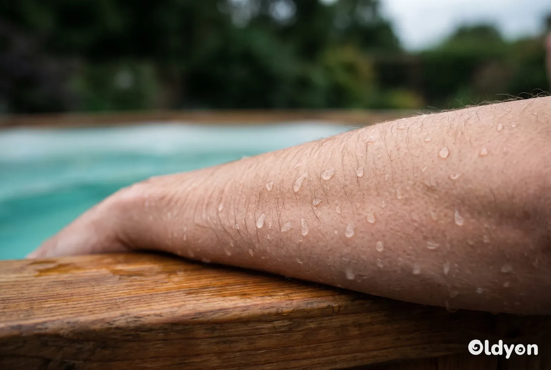 Waterdruppels die aan de fijne haartjes op de arm van een persoon kleven die bij een houten hottub rust.