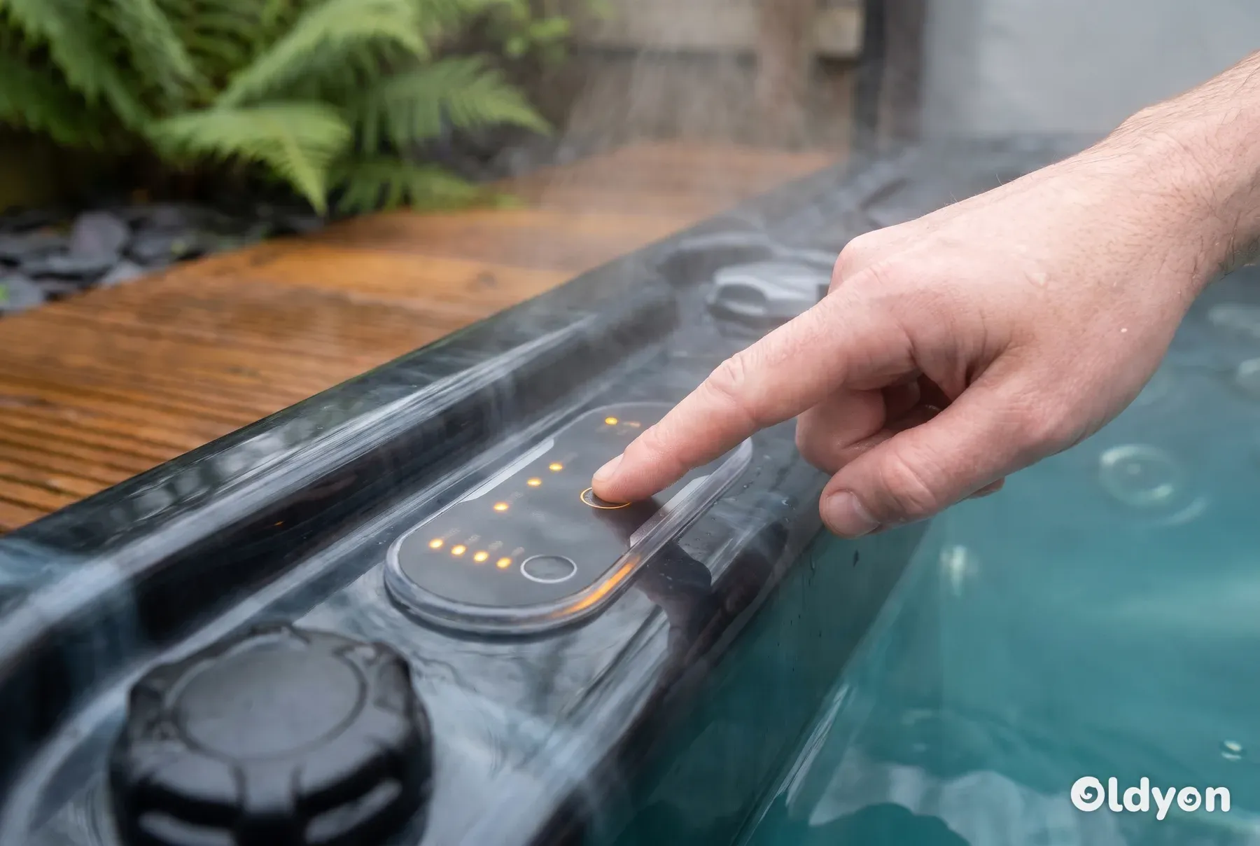 En våd finger trykker på en umarkeret, oplyst knap på et kontrolpanel til et spabad omgivet af damp.