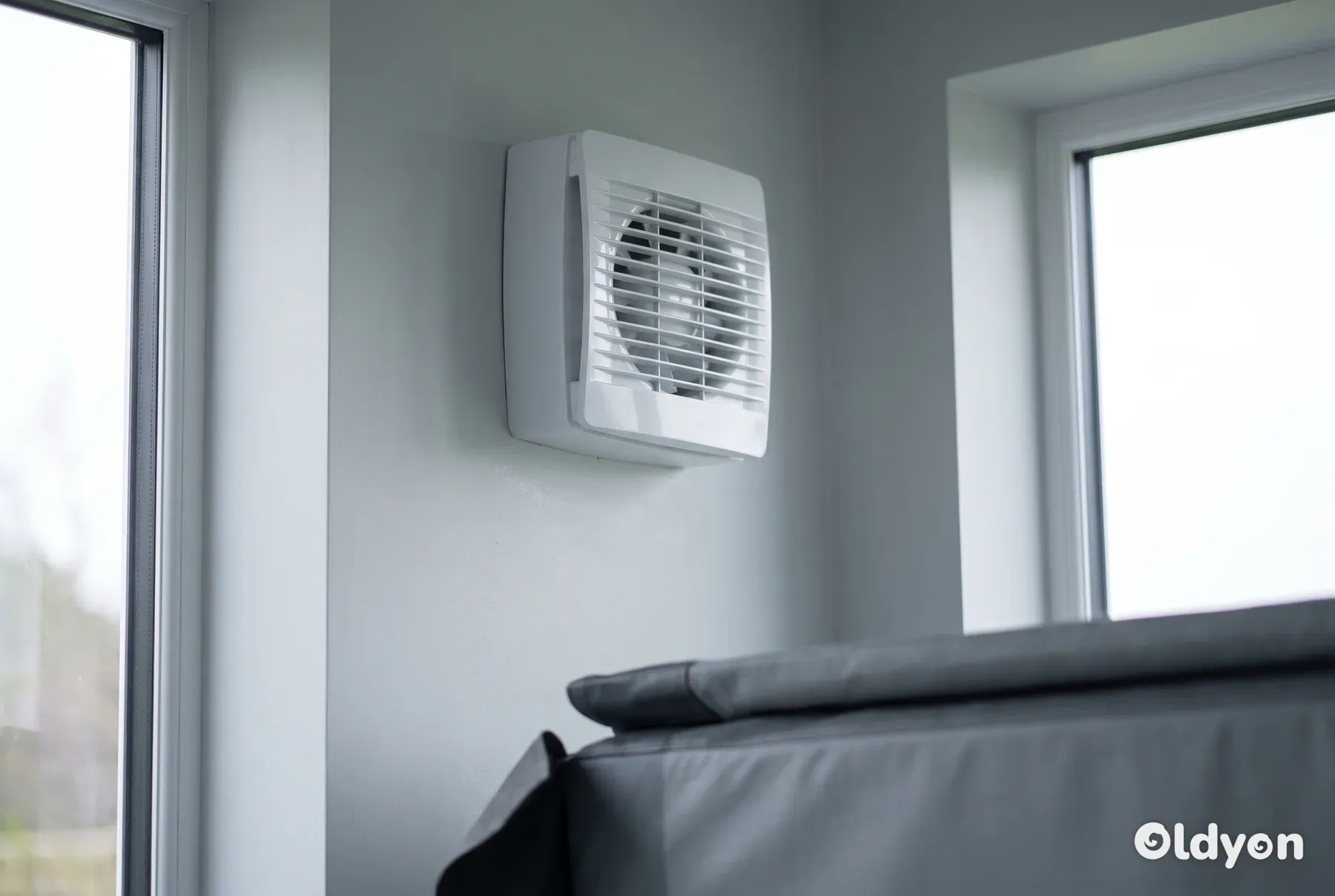 En moderne hvid udsugningsventilator er monteret højt oppe på en lysegrå væg over et spabad.
