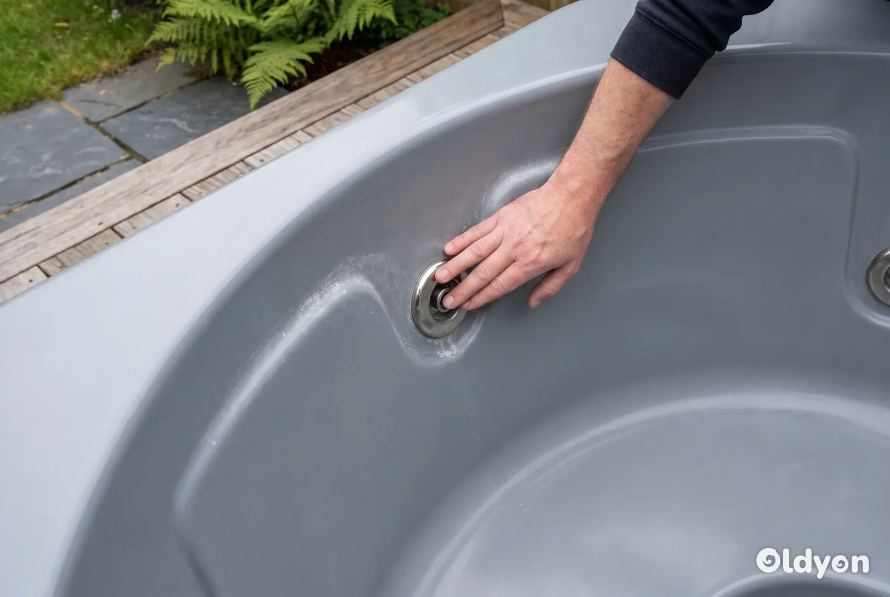 Een hand inspecteert een roestvrijstalen jet van een hottub die lichte tekenen van kalkaanslag en slijtage vertoont.