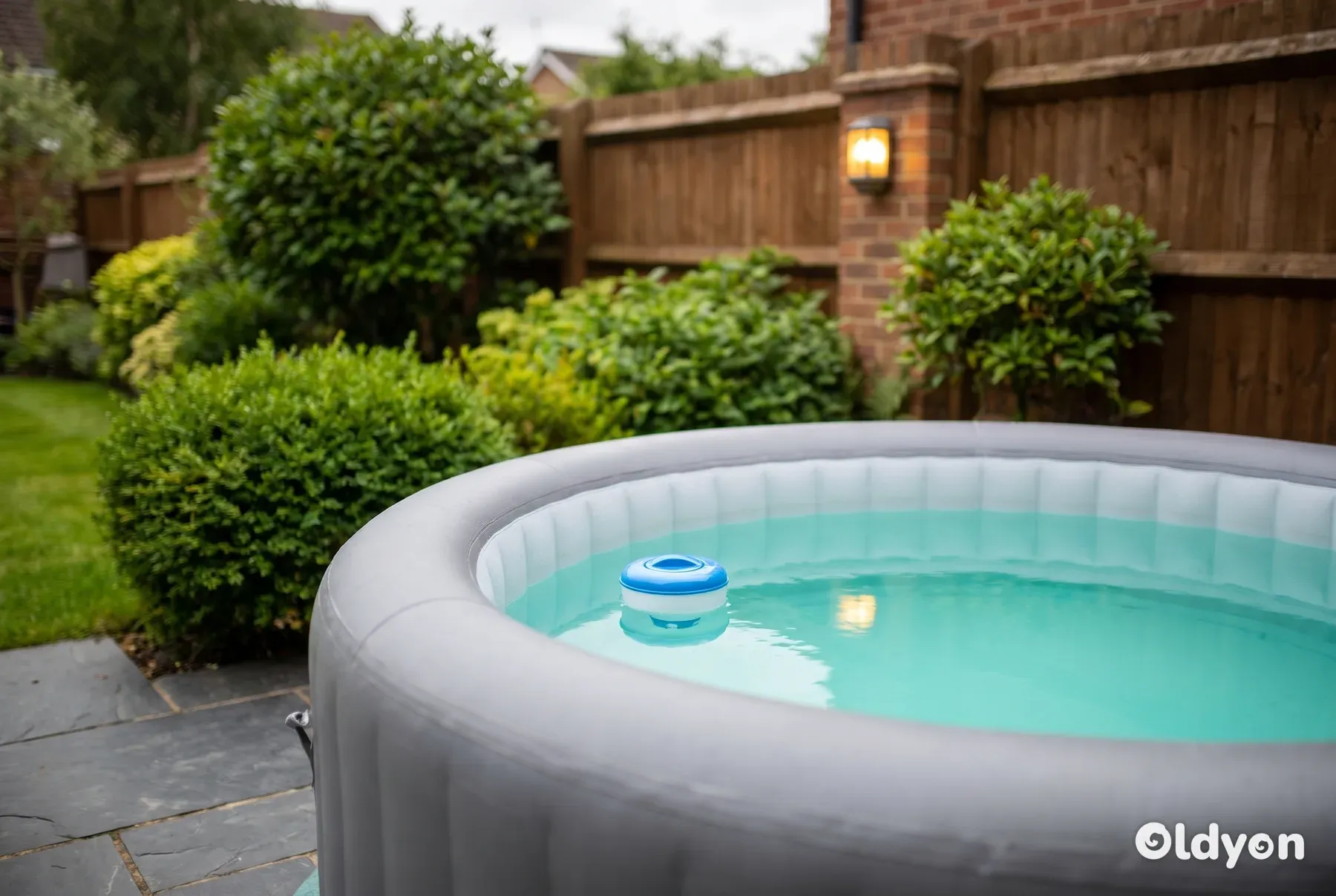 Een grijze opblaasbare hottub staat op een leistenen terras met een drijvende chemicaliëndispenser erin.
