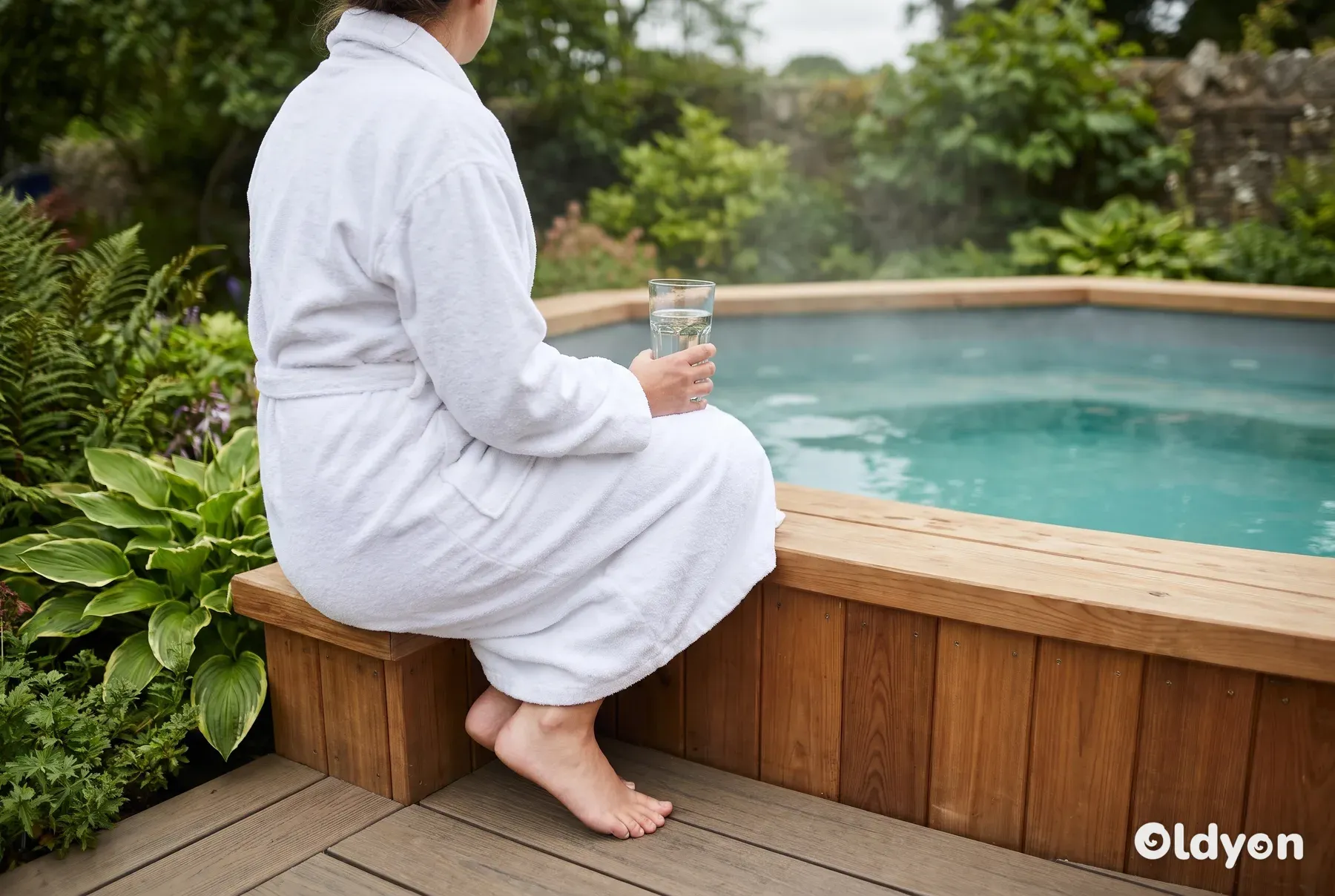 En person sidder på trækanten af en dampende spa og køler af med drikkevand.
