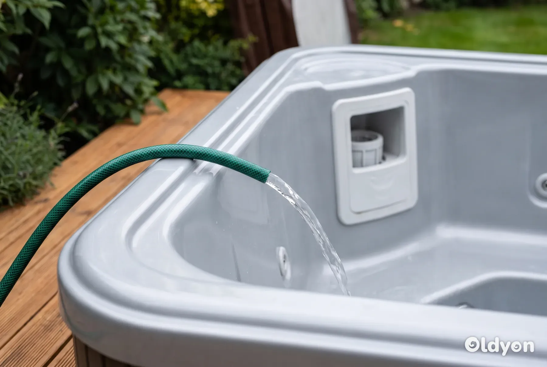 Een groene tuinslang vult een pas gereinigde en lege hottub met een straal water.