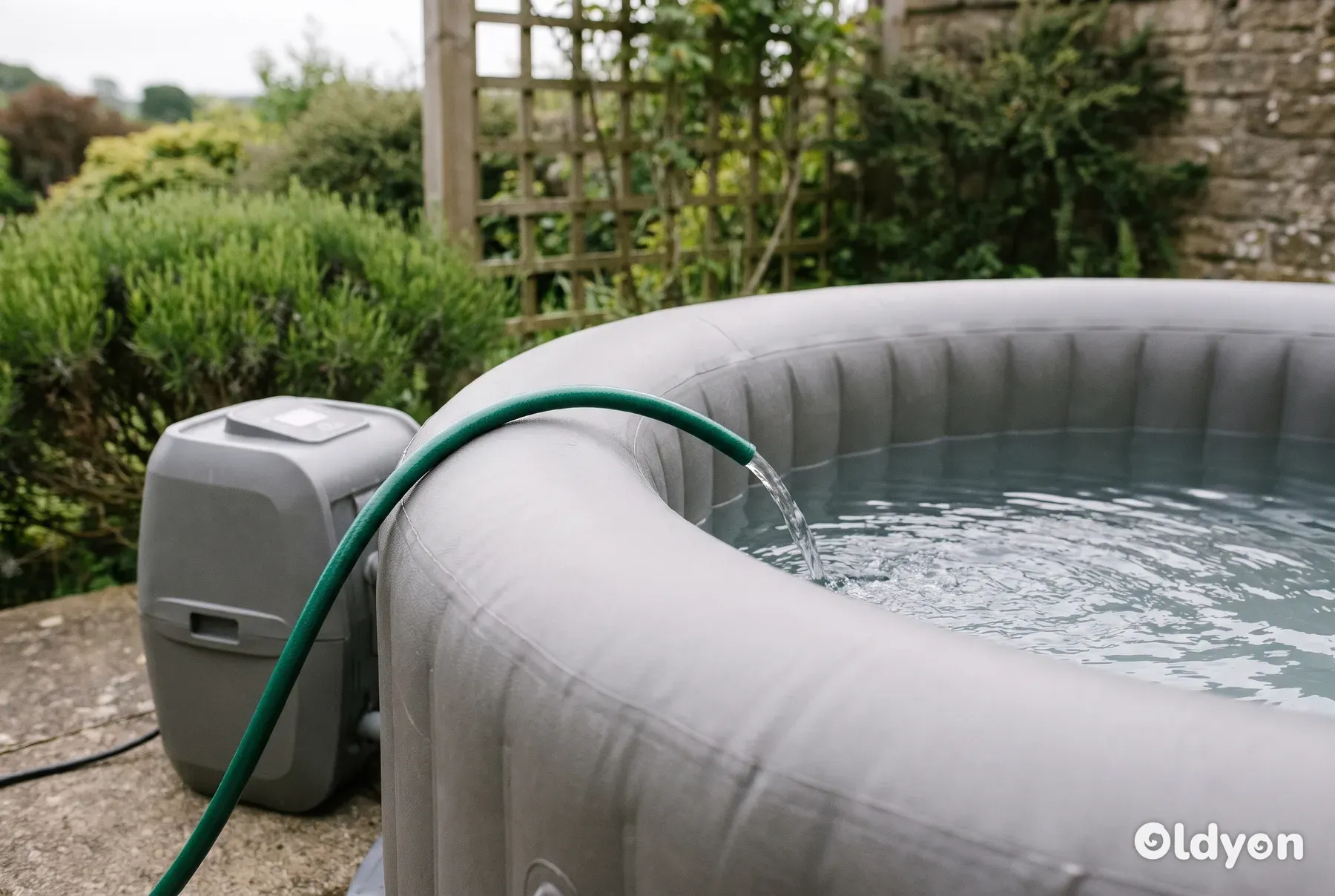Una minipiscina gonfiabile grigia su un patio in cemento viene riempita d'acqua con un tubo da giardino.