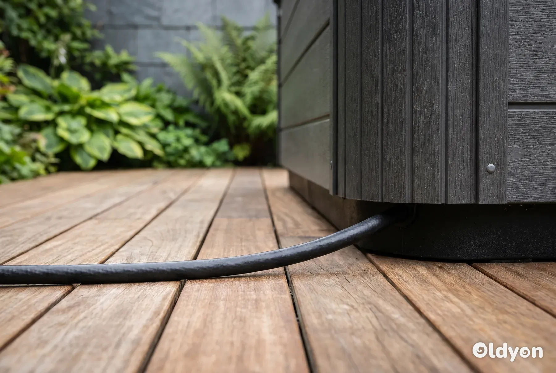 Un grosso cavo di alimentazione nero corre ordinatamente lungo un decking in legno da giardino verso la base di una minipiscina.