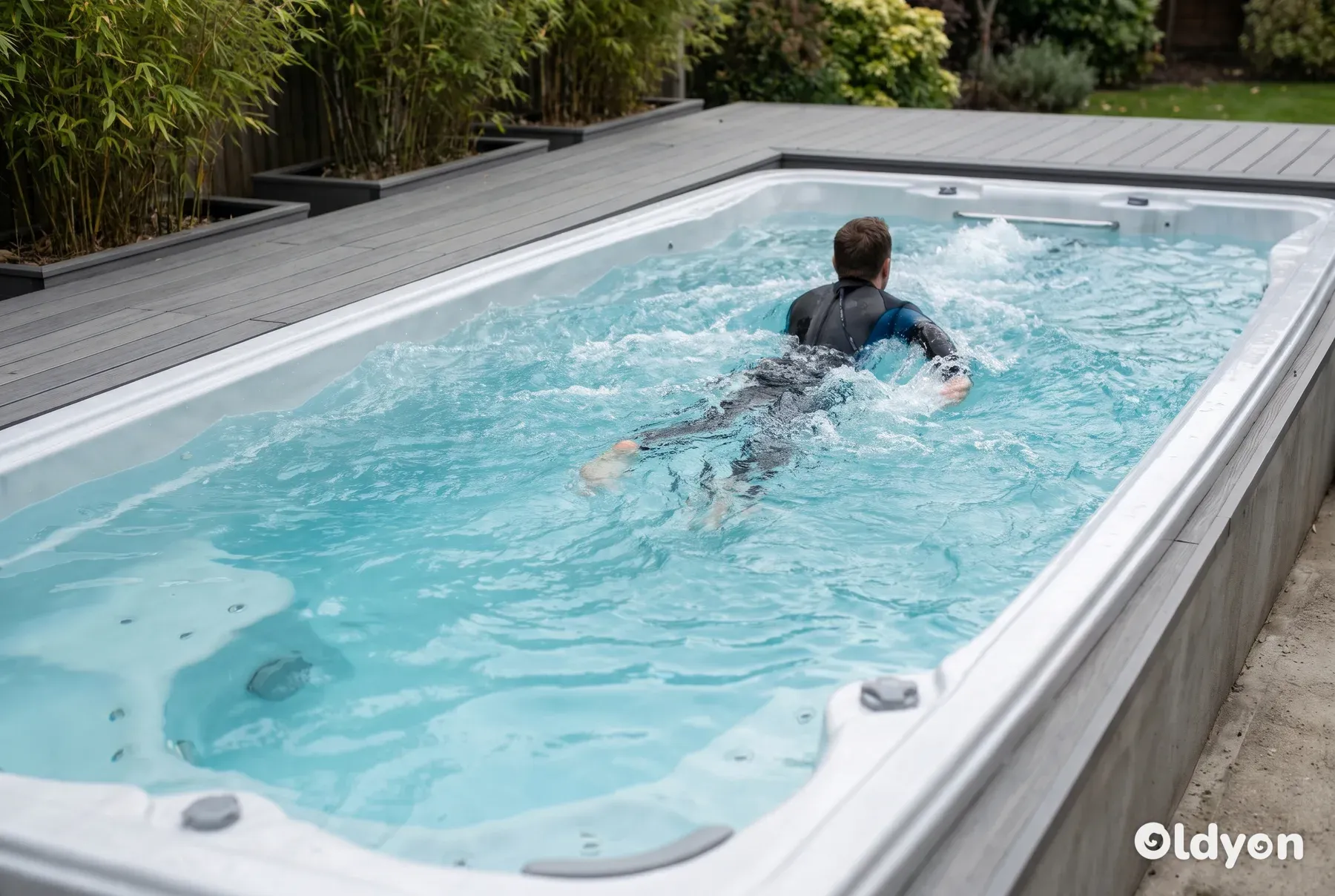 Una persona nuota contro la forte controcorrente in una lunga swim spa rettangolare su un decking in composito.