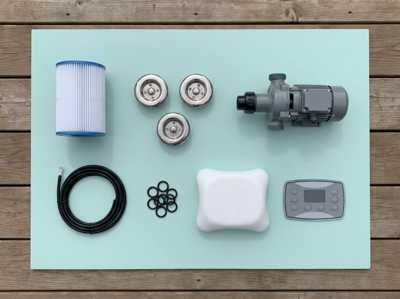 Hot tub parts laid out on a deck: a filter cartridge, jets, a pump, O-rings, a headrest pillow and a control panel.